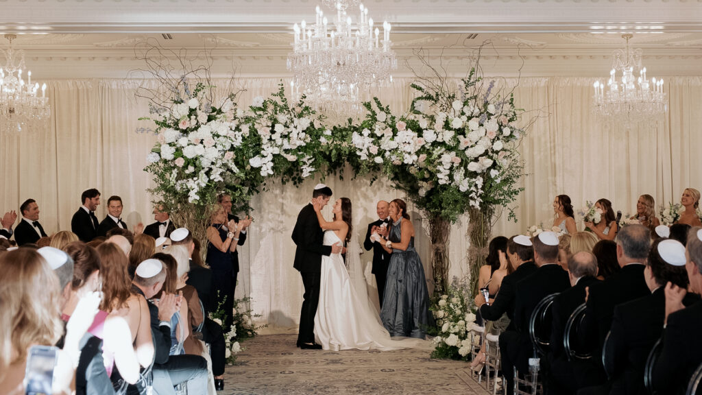 Bride and groom standing under a floral covered chuppah